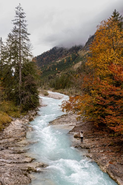 Free Explore a tranquil autumn river landscape with vibrant foliage and a lone figure, perfect for nature lovers. Stock Photo