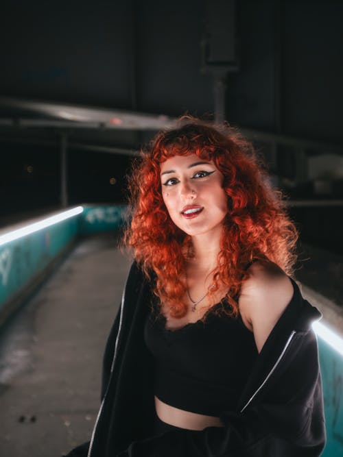 Young Redhead in a Black Outfit Standing on an Illuminated Footbridge 