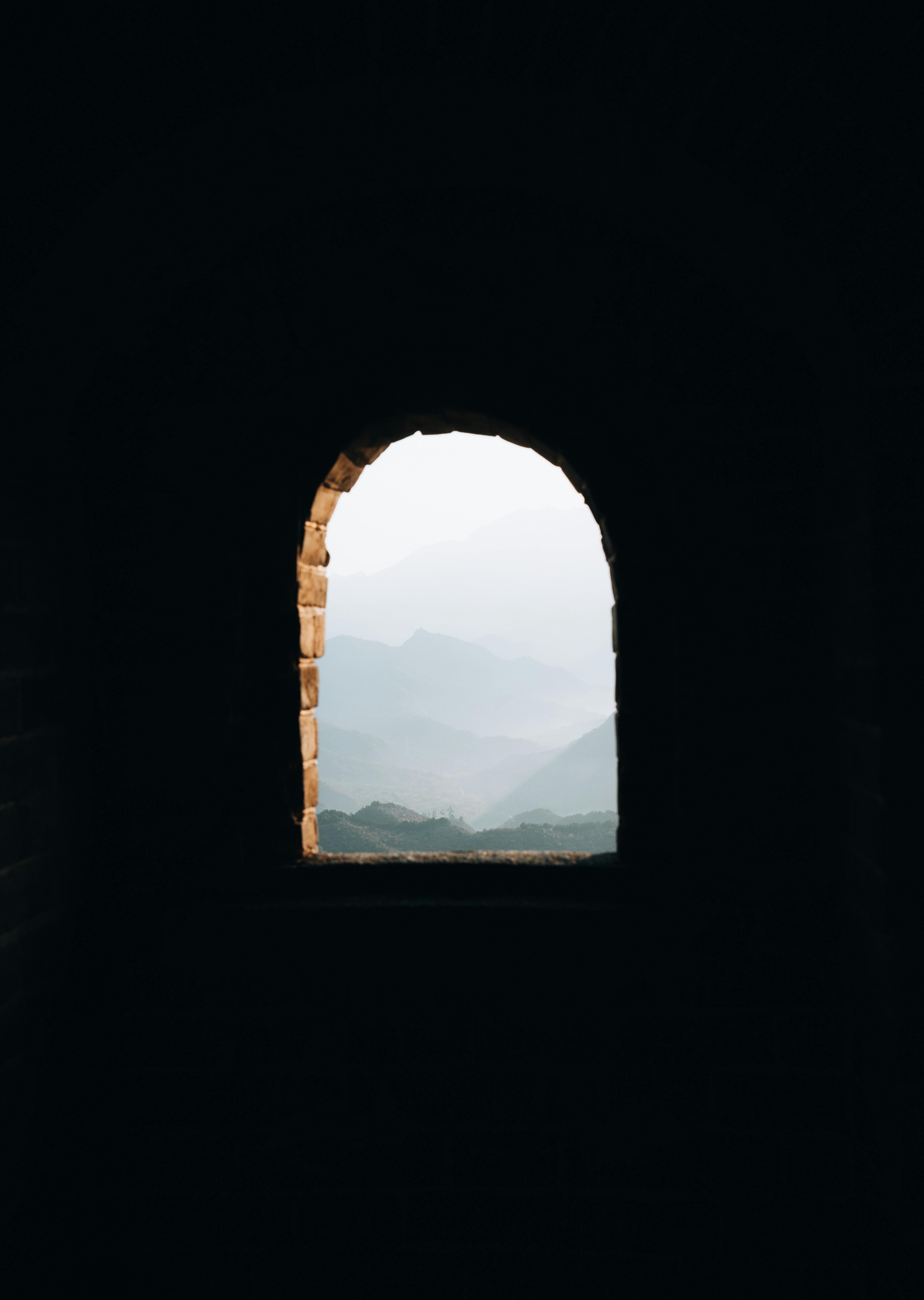 A serene view of misty mountains through an arched window in the Great Wall of China, showcasing natural beauty.