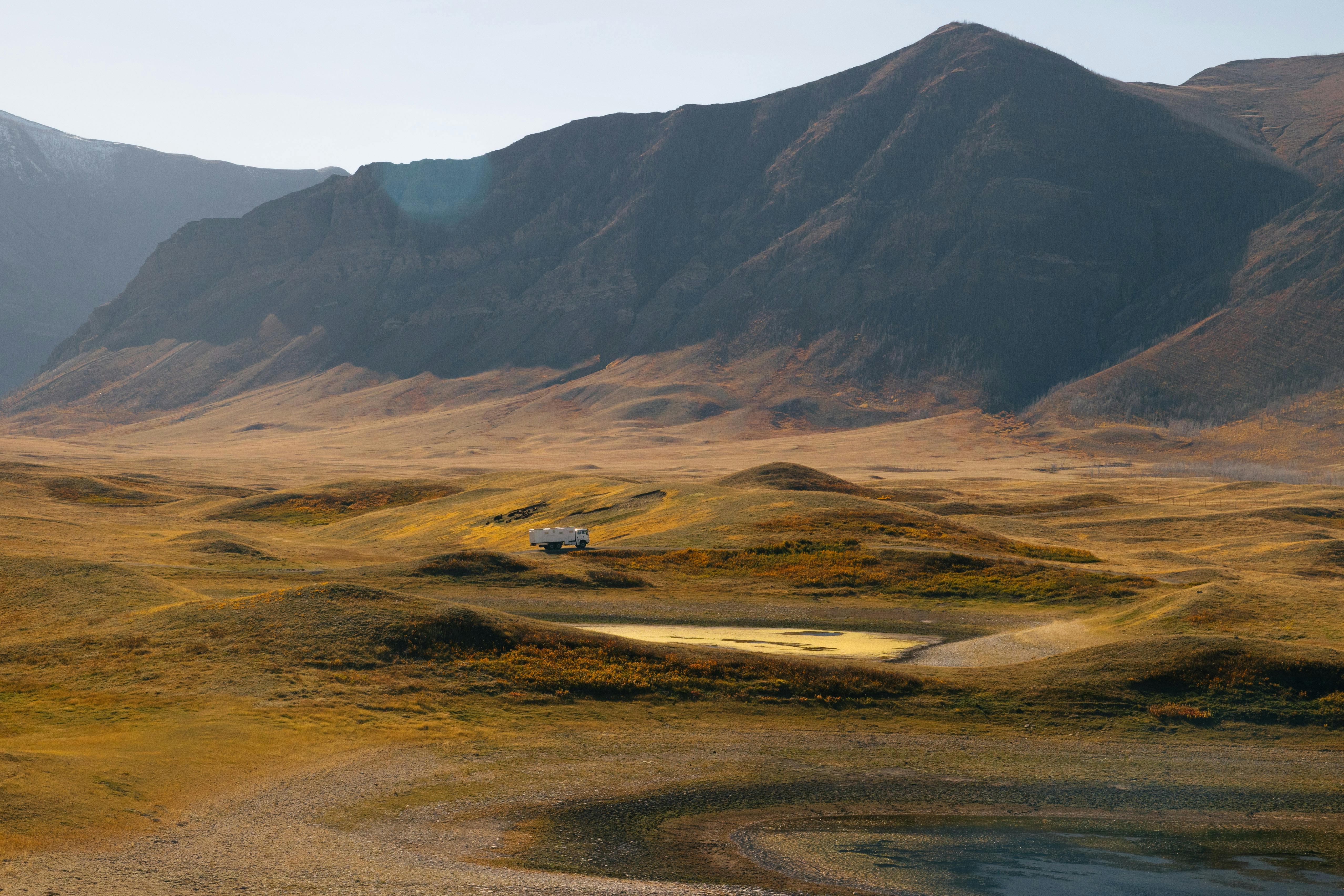 A truck parked in a vast mountain landscape under clear blue skies, showcasing rugged wilderness and isolation.