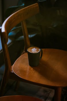 A stylish mug with latte art sits on a wooden chair in an Ankara cafe, creating a warm, inviting atmosphere.