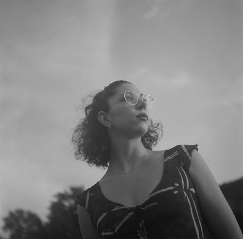 Free Artistic black and white portrait of a woman standing outdoors, wearing eyeglasses. Stock Photo