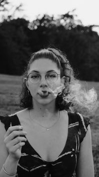 A striking black and white portrait of a woman smoking in an outdoor setting.