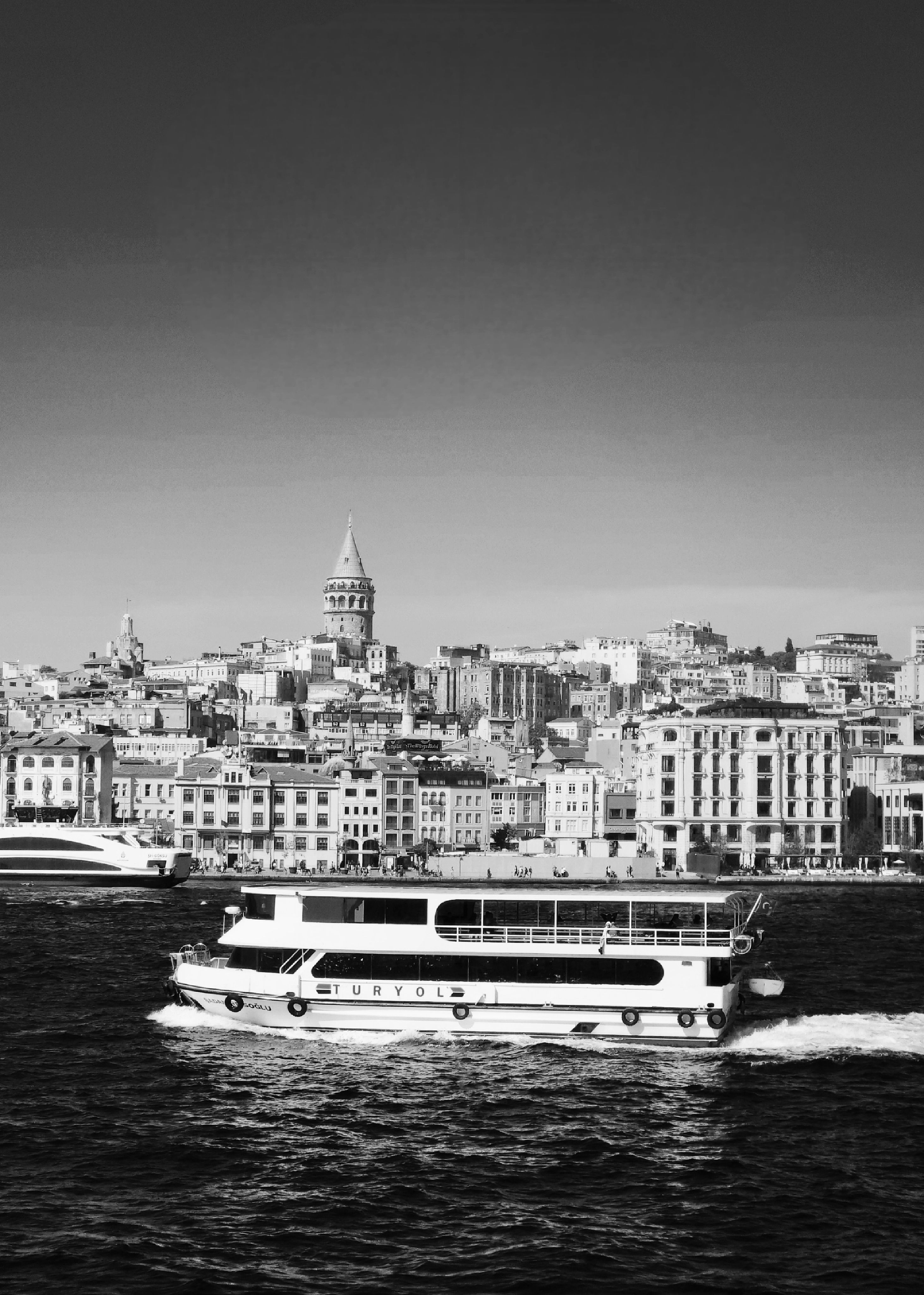 Black and white view of a ferry crossing the Bosphorus with Galata Tower in the background, Istanbul.