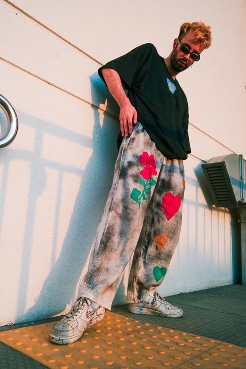 Free Fashion-forward individual in bold streetwear with colorful painted pants under warm sunlight. Stock Photo