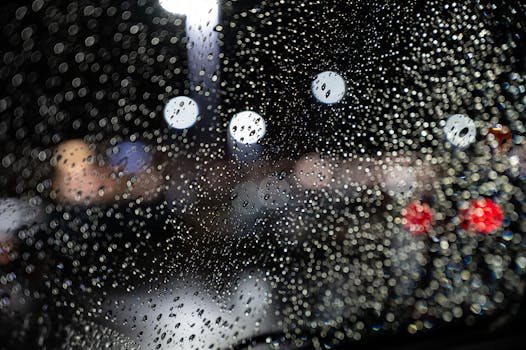 夜晚，挡风玻璃上清晰的雨滴映衬着背景中彩色的散景灯光