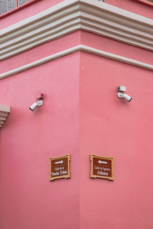 Corner of a Pink Building with Surveillance Cameras and Street Name Signs