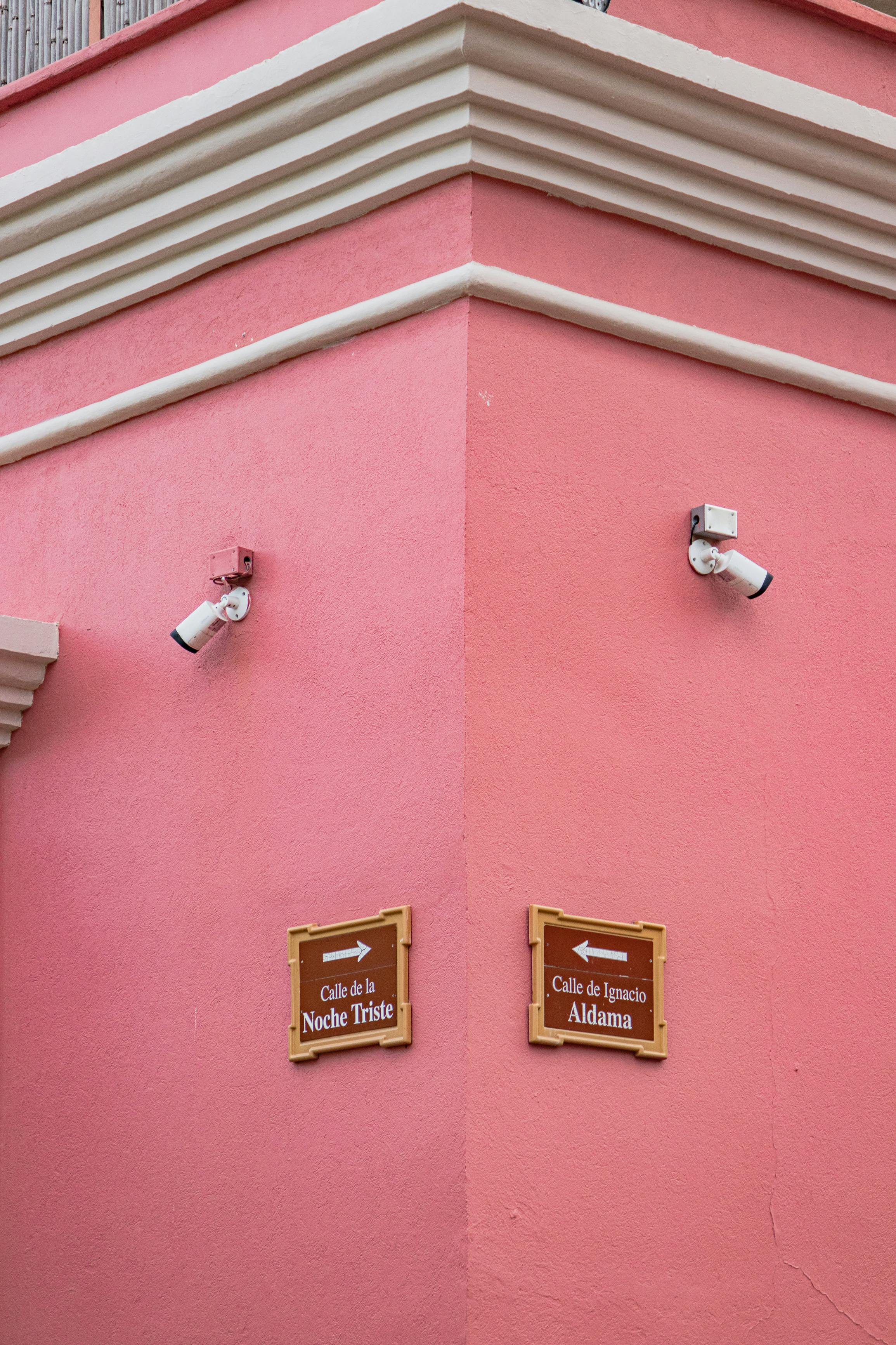 Free Pink building corner with street signs 'Calle de la Noche Triste' and 'Calle de Ignacio Aldama', featuring surveillance cameras. Stock Photo