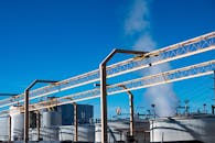 工业工厂视野开阔，储罐中升起的烟雾映衬着晴朗的蓝天