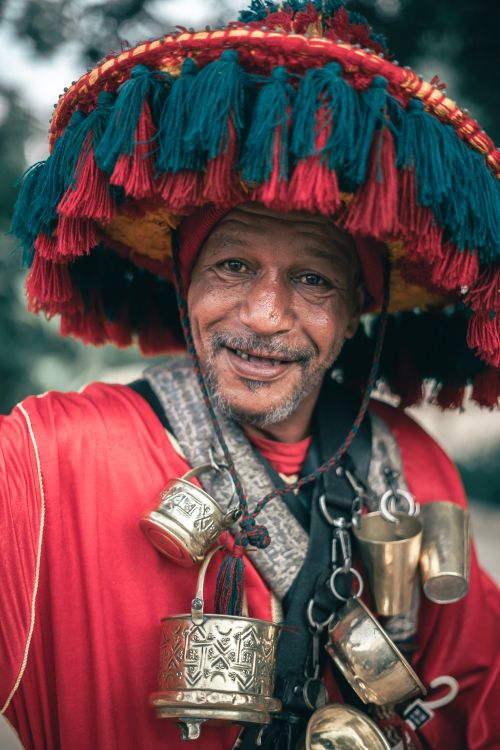 Free Portrait of an elderly man wearing traditional red and gold clothing with a tassel hat and decorative bells. Stock Photo