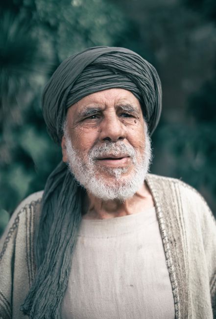 Elderly man with a beard and turban, wearing traditional clothing outdoors.