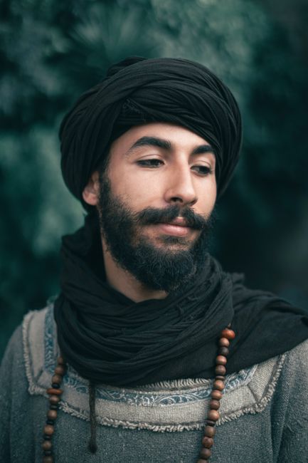 Intimate portrait of a man wearing a turban, scarf, and beaded necklace, showcasing cultural style and fashion.