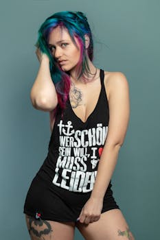 Woman in black tank top with tattoos, colorful hair, and expressive pose indoors.