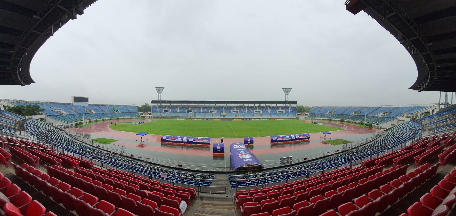 Wide-angle shot of an empty sports stadium under gloomy skies, highlighting the red and blue seating areas.