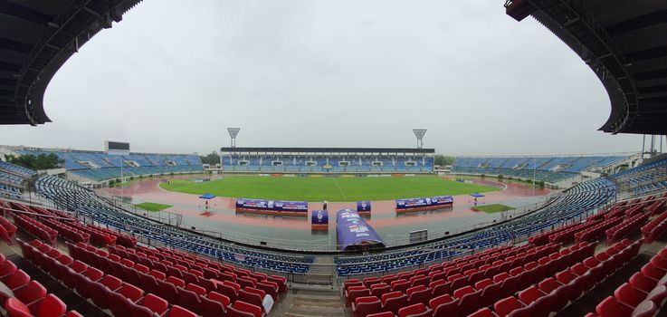 Wide-angle shot of an empty sports stadium under gloomy skies, highlighting the red and blue seating areas.