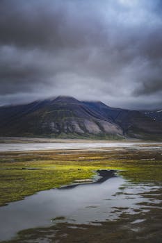 A dramatic mountain scene with rain clouds and a reflective puddle in a barren landscape.
