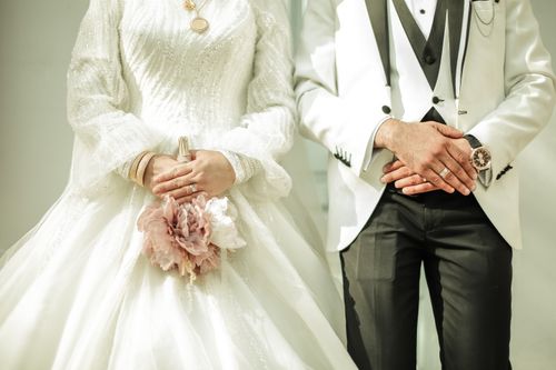 Free Close-up of a bride and groom in elegant wedding attire with bouquet and wristwatch detail. Stock Photo