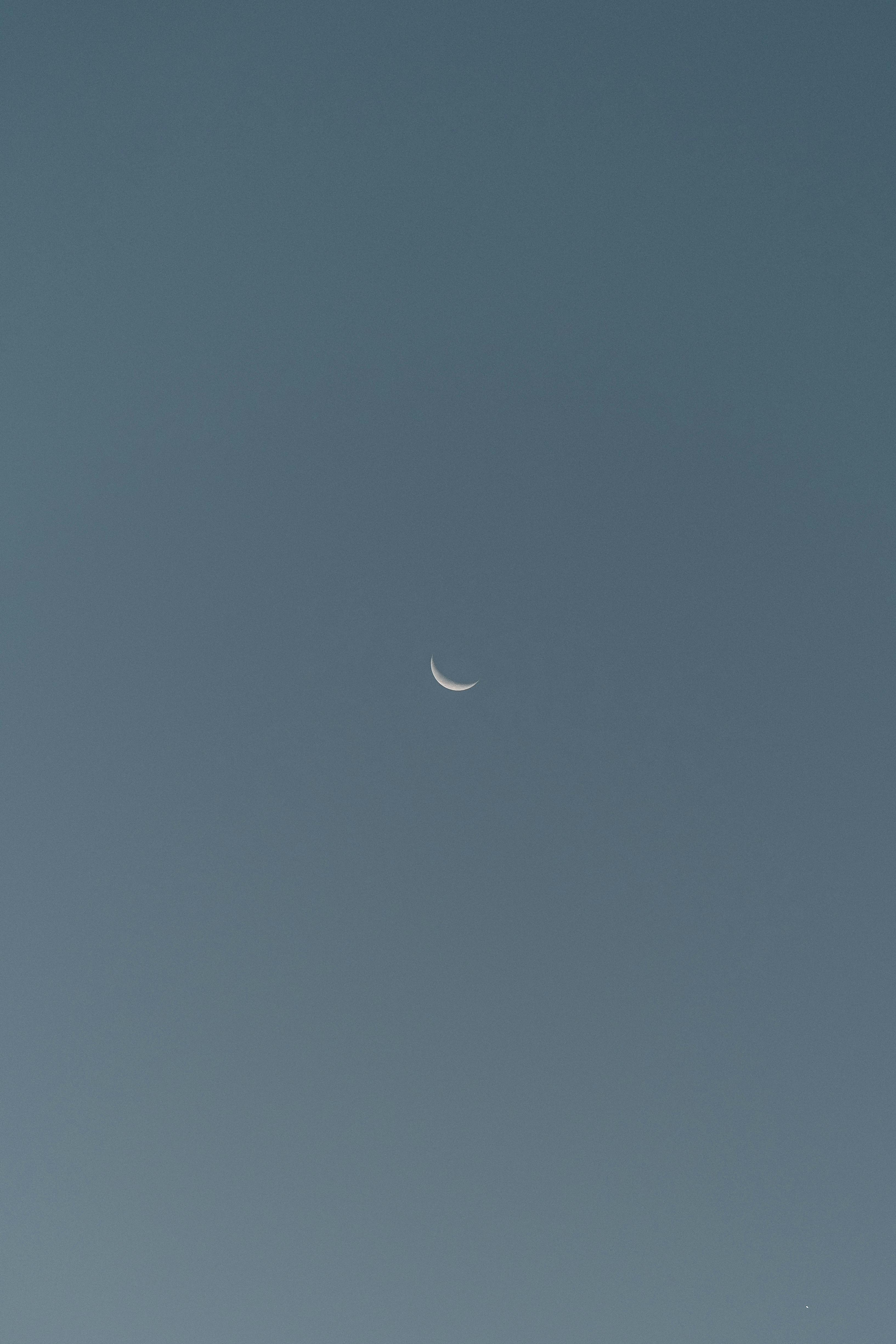 Serene crescent moon against a clear blue evening sky, evoking tranquility.