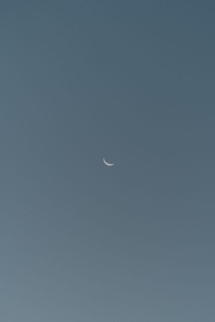 Serene crescent moon against a clear blue evening sky, evoking tranquility.