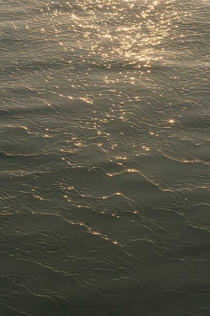 Sunlight sparkles on gentle sea waves, creating a serene and mesmerizing scene.
