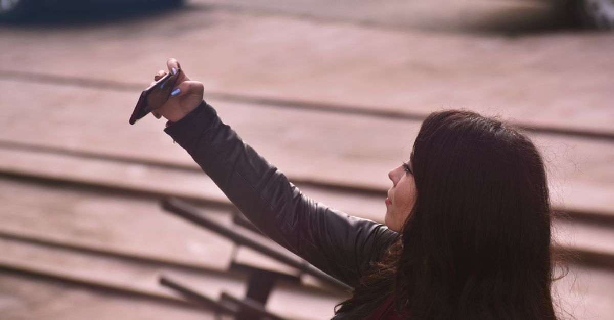 A young woman takes a selfie with her smartphone in an outdoor setting, capturing a moment of joy.