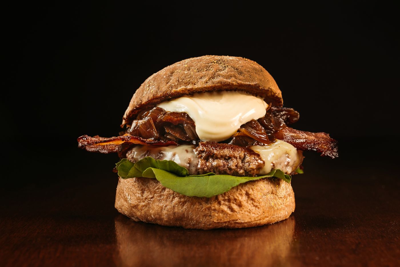 A stacked burger with bacon and melted cheese on a dark backdrop. Photo by Jonathan Borba on Pexels.
