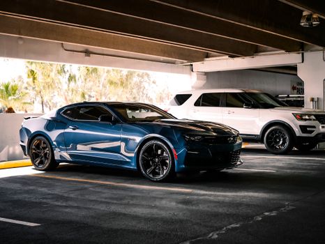 Luxurious blue sports car parked indoors beside a white SUV in urban garage setting.