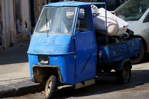 Free A weathered blue three-wheeler rickshaw parked on a city street, filled with clutter. Stock Photo