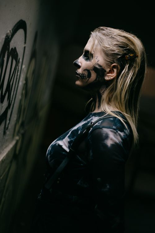 Free Woman with skull makeup standing by a graffiti-adorned wall, embodying Halloween punk style. Stock Photo