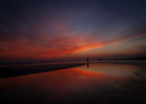 Free A lone person walks along a tranquil beach at sunset, reflected in tidal pools. Stock Photo
