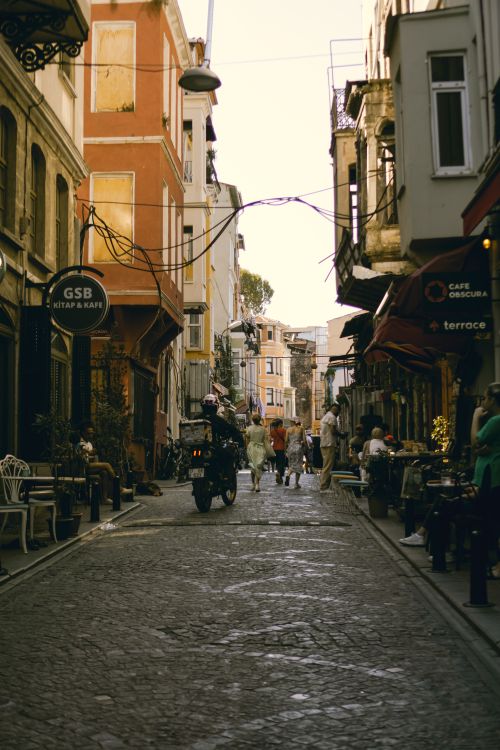 Free A picturesque cobblestone street lined with cafes, people, and a motorcycle. Stock Photo