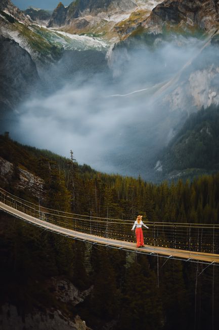 A breathtaking view of a woman on a suspension bridge set against a mountainous landscape shrouded in mist.