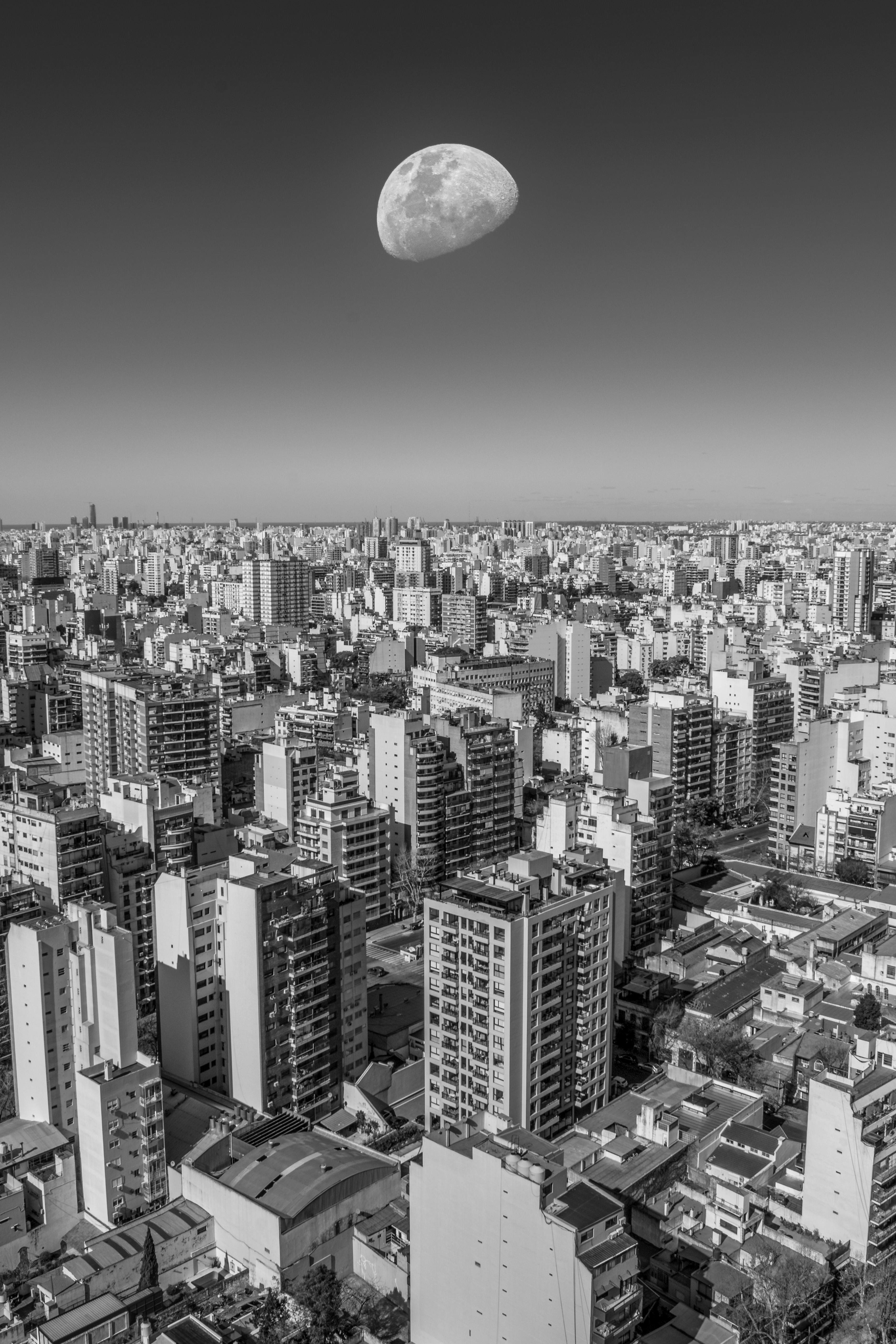 Dramatic black and white aerial view of Buenos Aires cityscape with a large moon overhead.