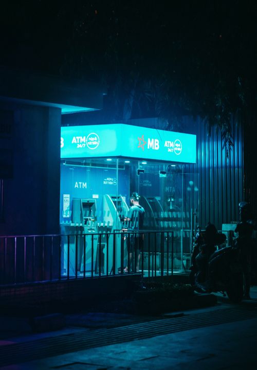 Free Person using ATM at night, illuminated by vibrant neon lights, in an urban setting. Stock Photo