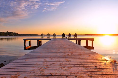 Back of a Person Sitting Alone at the Edge of a Wooden Jetty at Sunset