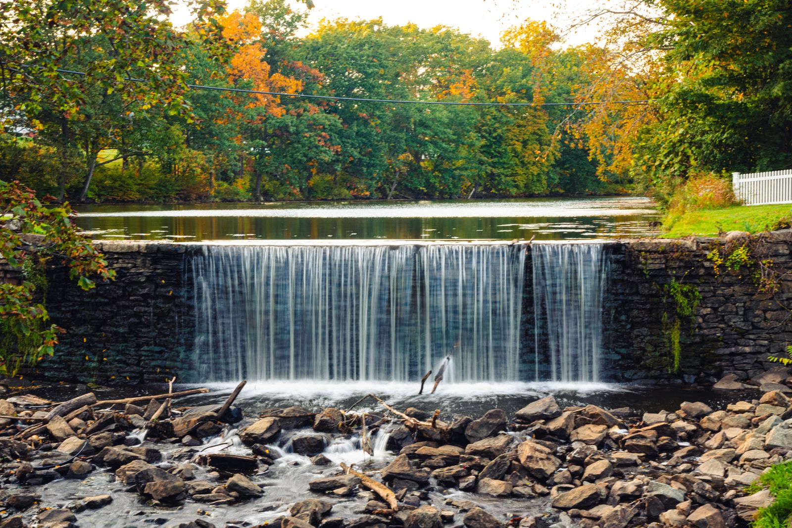 A small waterfall in a park surrounded by colorful autumn foliage