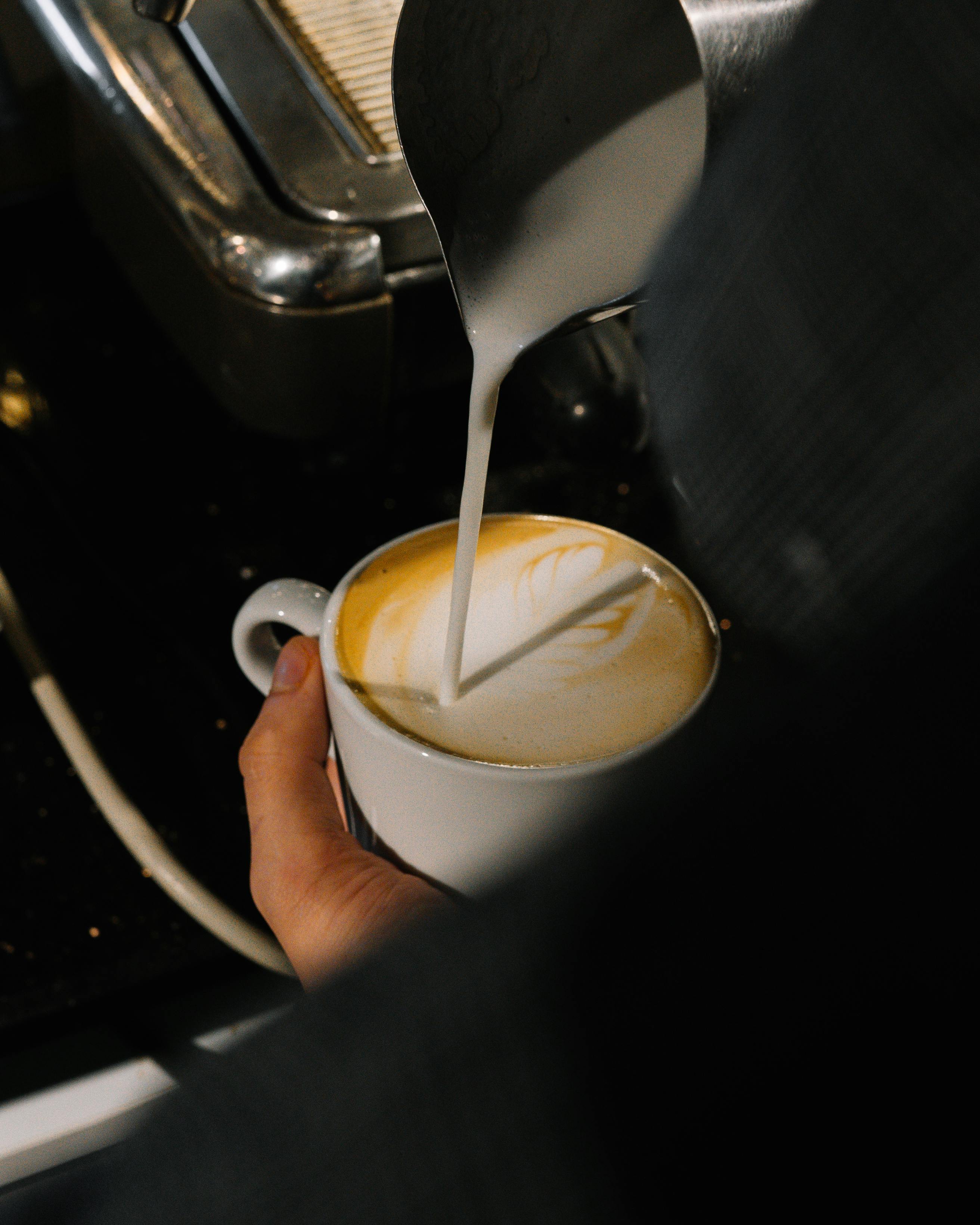 Close-up of barista pouring milk to create latte art in a coffee shop setting.