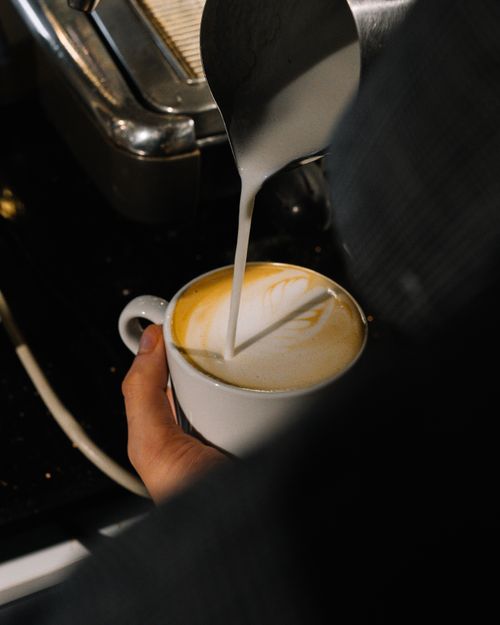 Free Close-up of barista pouring milk to create latte art in a coffee shop setting. Stock Photo