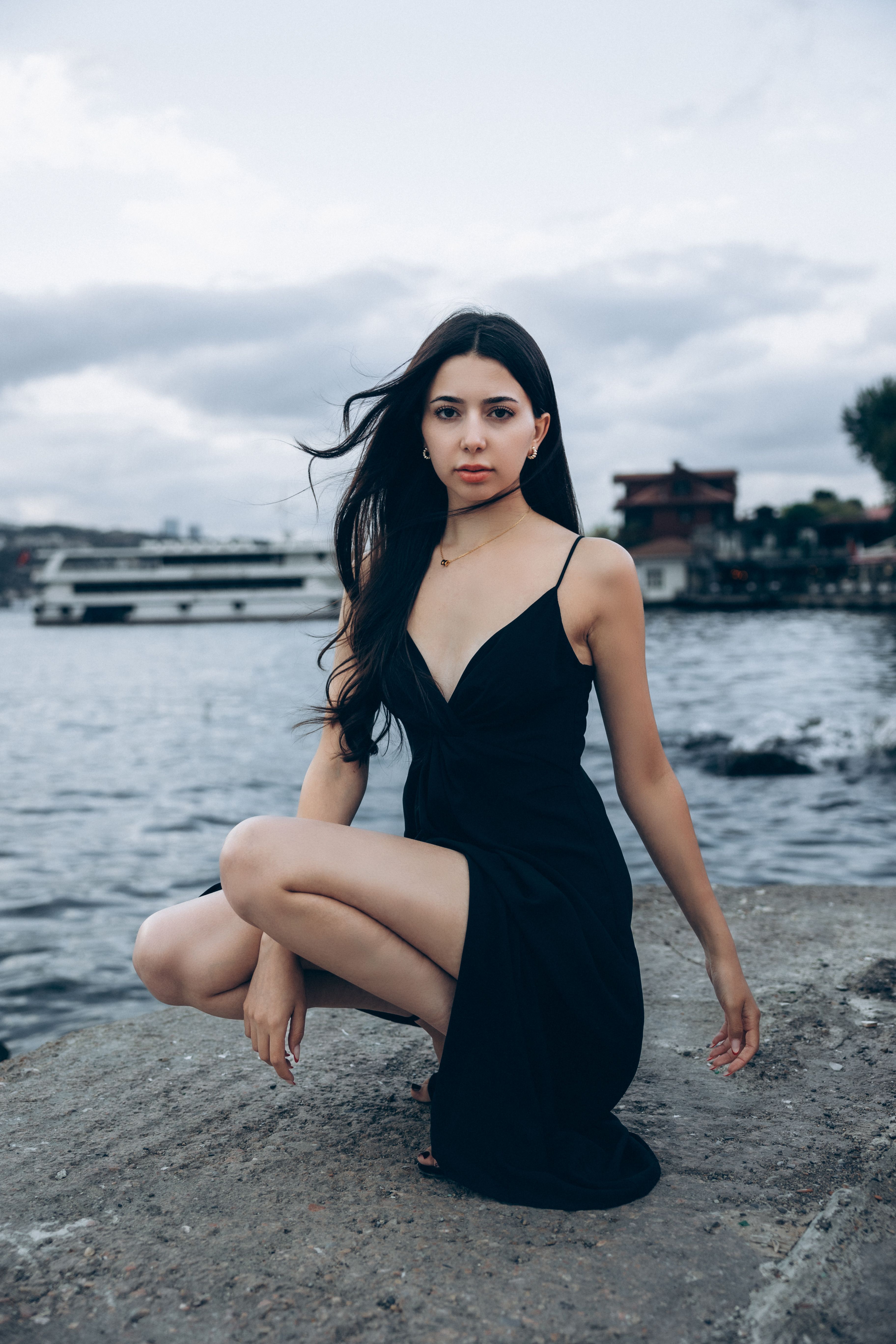 A woman in a black dress sitting on the ground near water · Free Stock ...