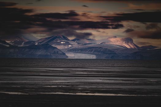 Stunning twilight scene with rugged mountains and dramatic clouds over a tranquil water body.
