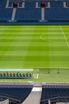 A vertical view of an empty soccer stadium in Porto, Portugal. Sunlight casts shadows on the green field.