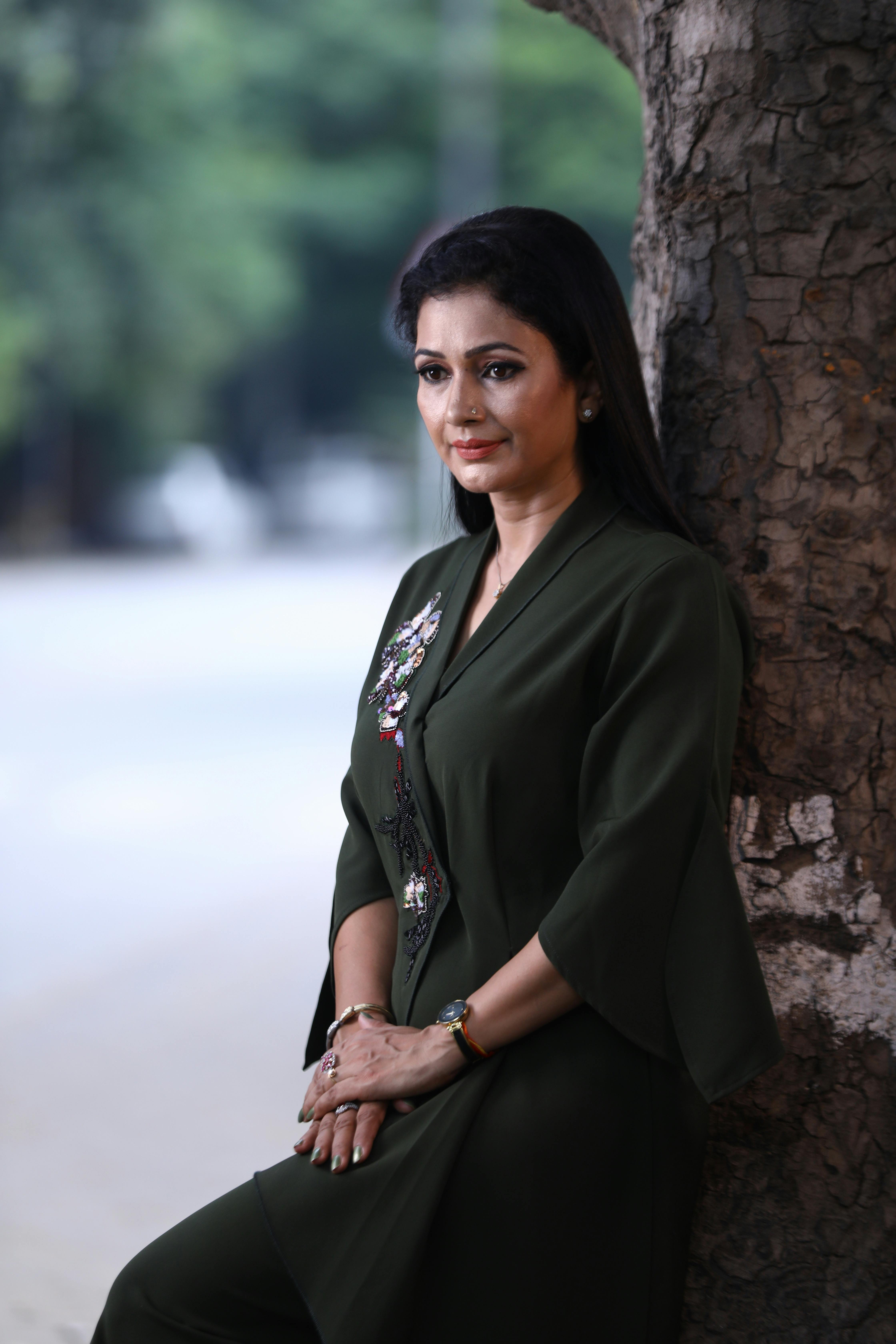 Elegant woman with black hair posing outdoors in green attire, embodying fashion and grace.