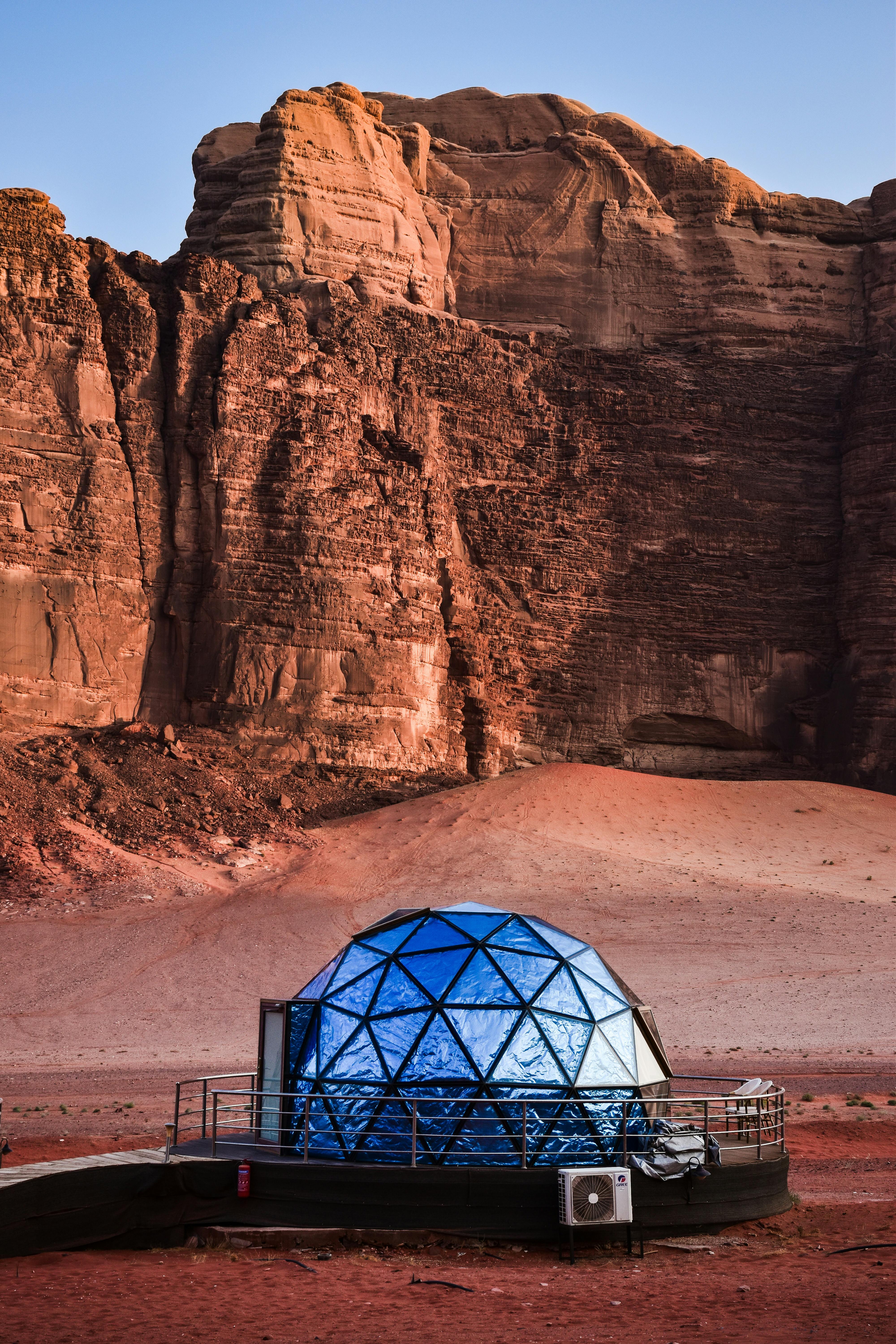 A futuristic glass dome structure in a barren, desert landscape with striking cliff formations.