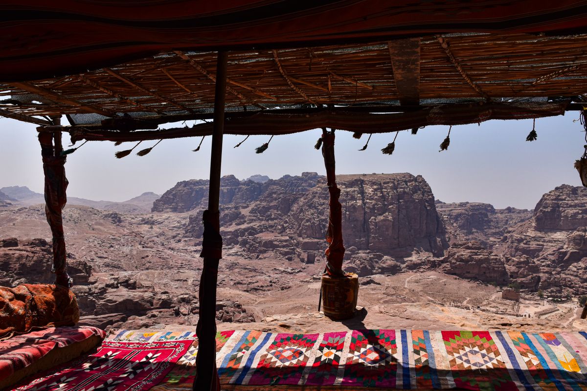 The view of Petra's rugged mountain landscape framed under a shaded shelter with colorful woven carpets