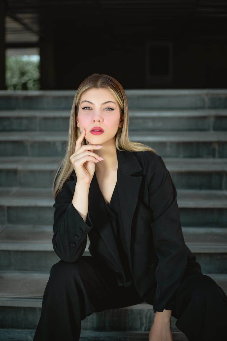 Elegant Blonde Woman In Black Suit Sits On Steps