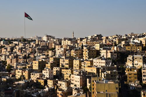Free A stunning aerial view of Amman's urban cityscape with the Jordan flag fluttering prominently. Stock Photo