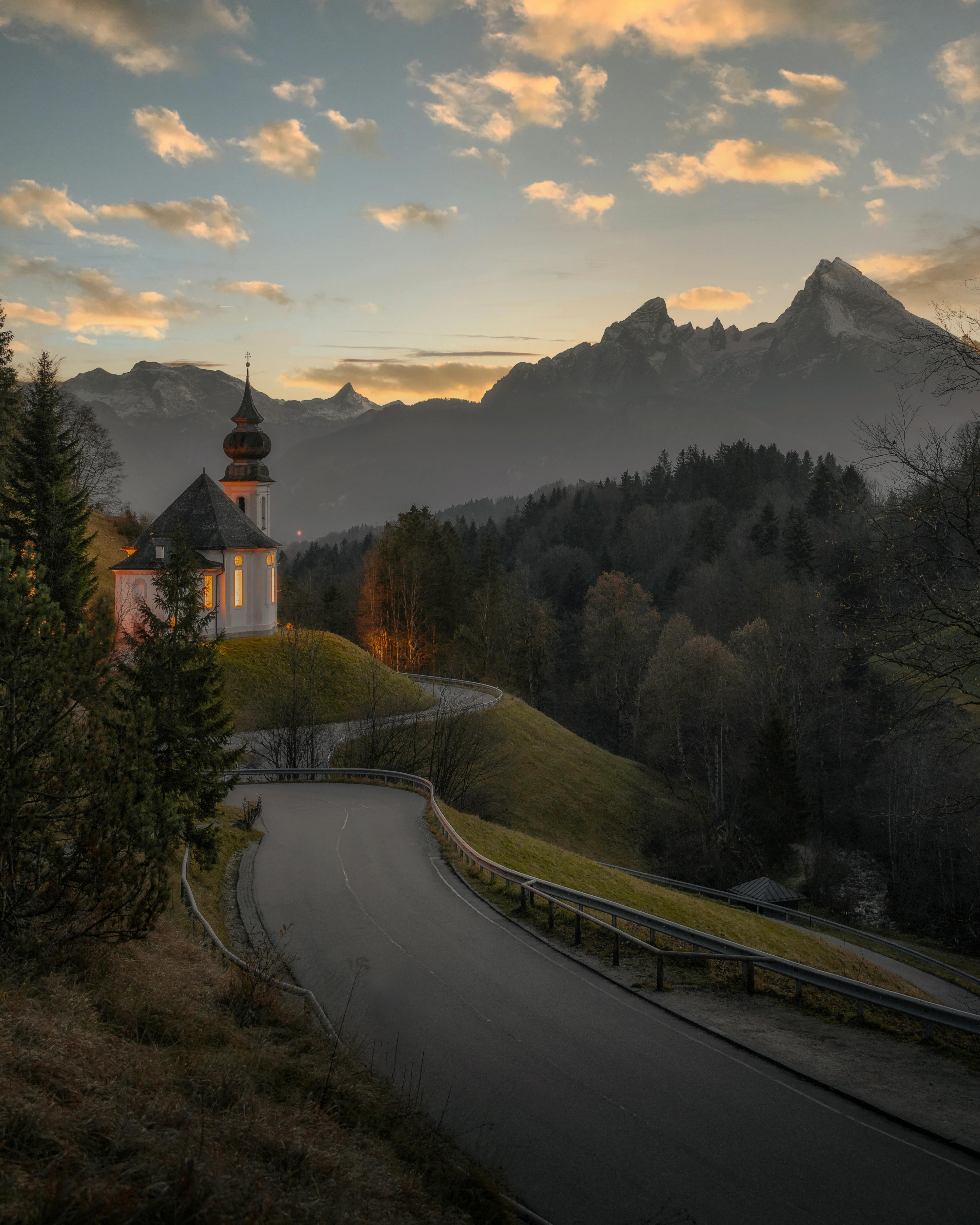 Serene view of a church at dawn surrounded by fog and mountains on a winding road.