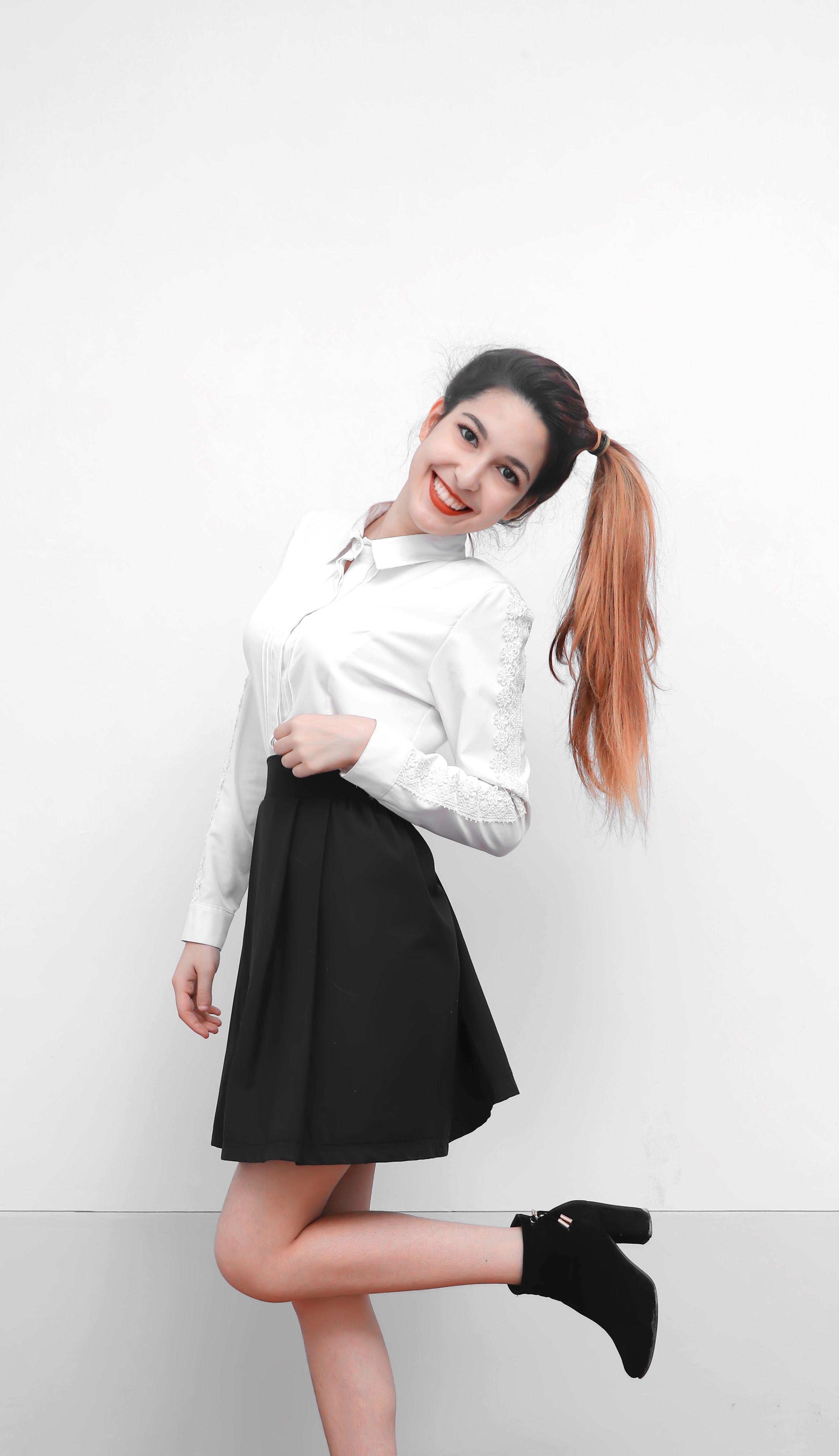 Smiling woman with brown hair in a white shirt and black skirt, posing on a white background.