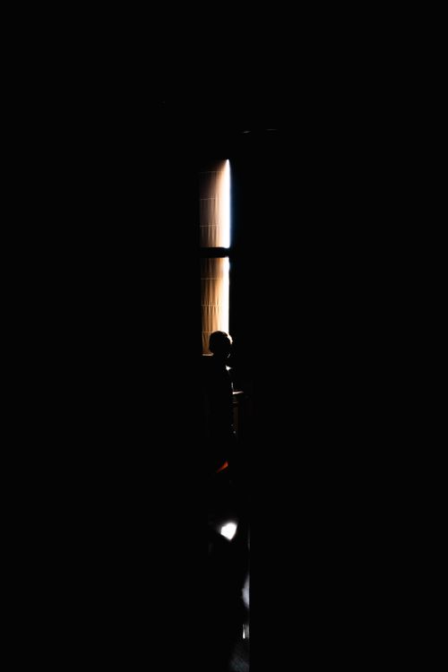 Free A mysterious silhouette gazes through a window in a dark interior setting. Stock Photo