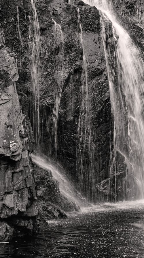 Free A dramatic black and white photograph capturing a waterfall cascading over rocky terrain. Stock Photo